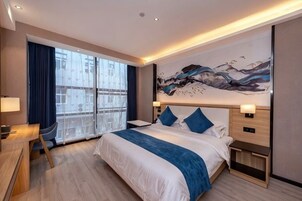 Una habitación de hotel moderna con una cama grande, mesitas de noche, un escritorio y vistas amplias por una ventana grande.