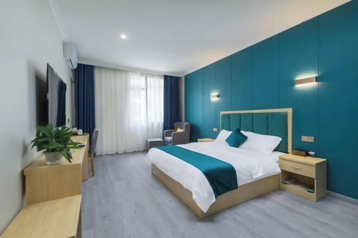 A modern hotel room with a large bed, a desk, a chair, and a TV.
