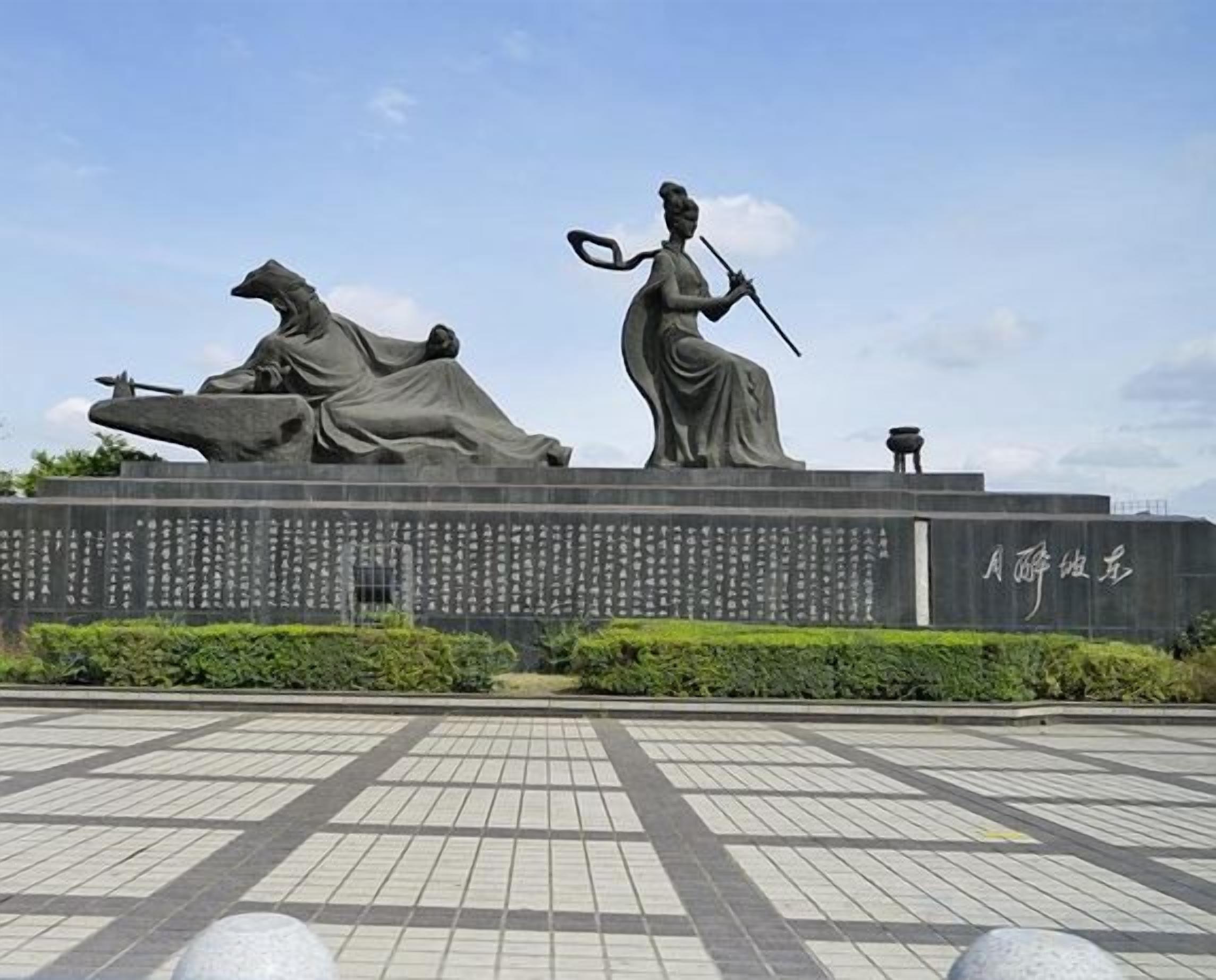 Un monumento con dos estatuas, una plaza empedrada y un muro con inscripciones.