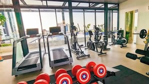 A gym with treadmills, stationary bikes, and weight machines. There are red dumbbells on a rack. - Studio Pollux Sea View Apartments

 (Batam City)