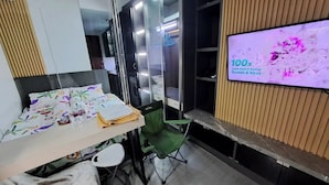 A hotel room with a bed, a desk with a chair, a television, and a wardrobe. - Studio Pollux Sea View Apartments

 (Batam City)