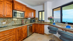 A modern kitchen with wooden cabinets, stainless steel appliances, granite countertops, and a large window offering a view of the ocean. - Oceanfront, Gound floor, Steps to the Beach!  (Cabo San Lucas)