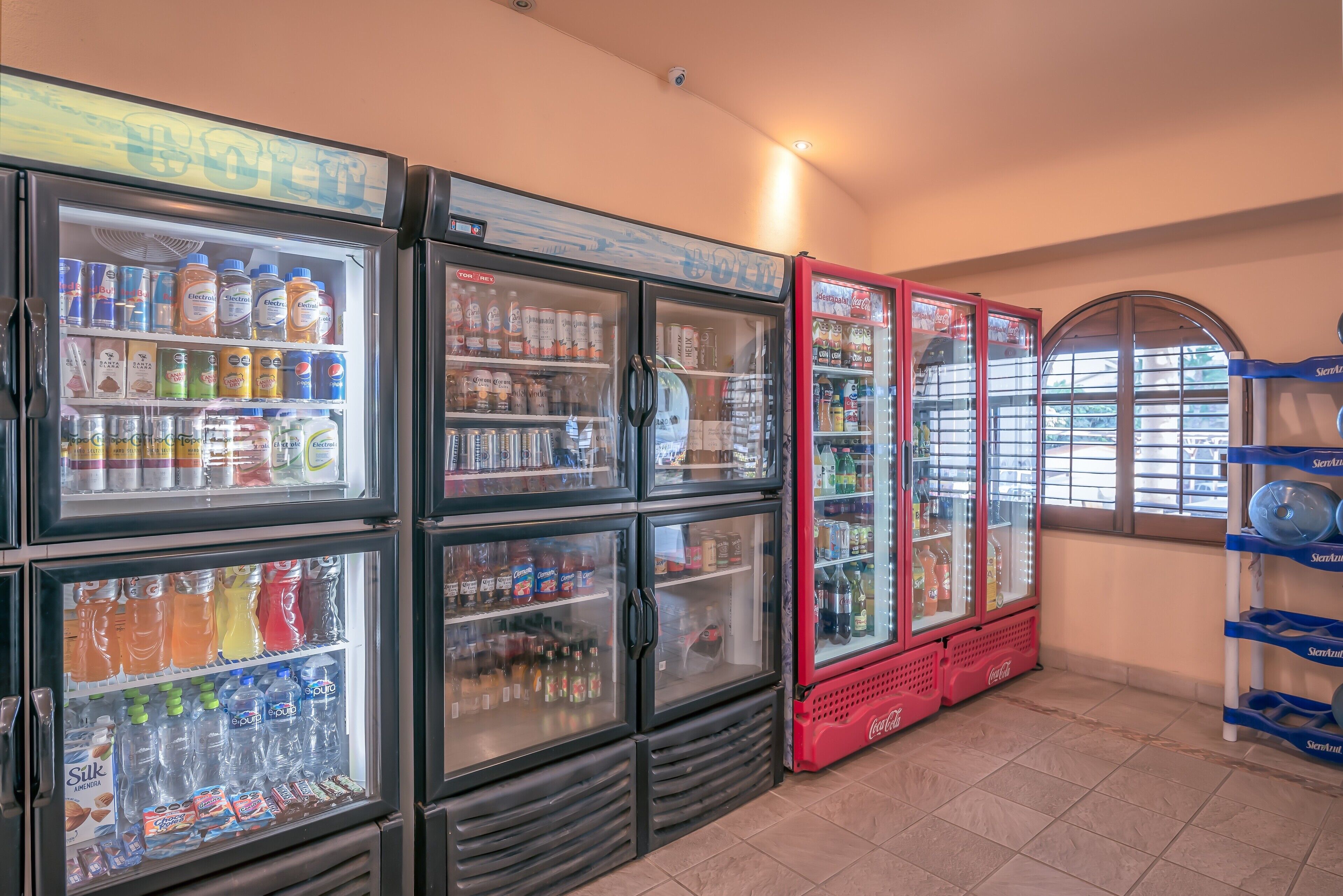 A row of beverage refrigerators stocked with various drinks, including sodas and juices, in a commercial setting.