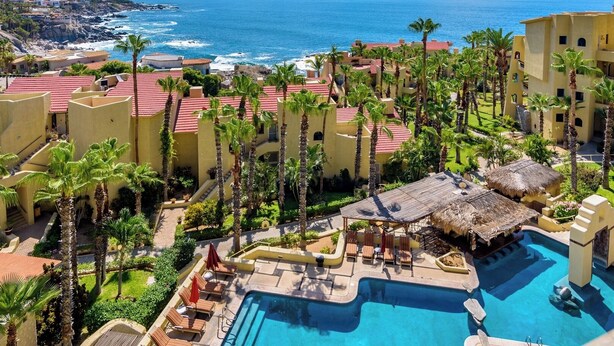 A resort with a swimming pool, palm trees, and a view of the ocean. - Oceanfront, Gound floor, Steps to the Beach!  (Cabo San Lucas)