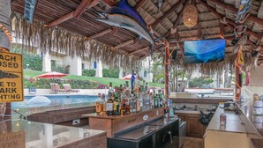 A bar area with a pool in the background, a thatched roof, and a sign indicating parking is closed. - Oceanfront, Gound floor, Steps to the Beach!  (Cabo San Lucas)