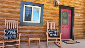 Une cabane en bois avec deux fauteuils à bascule, une porte rouge et une pancarte indiquant « Bienvenue ».