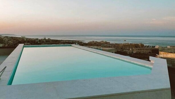 A rectangular swimming pool with a clear view of the sea and distant buildings. - So City Hotel - Adults Only (St. Julian's)