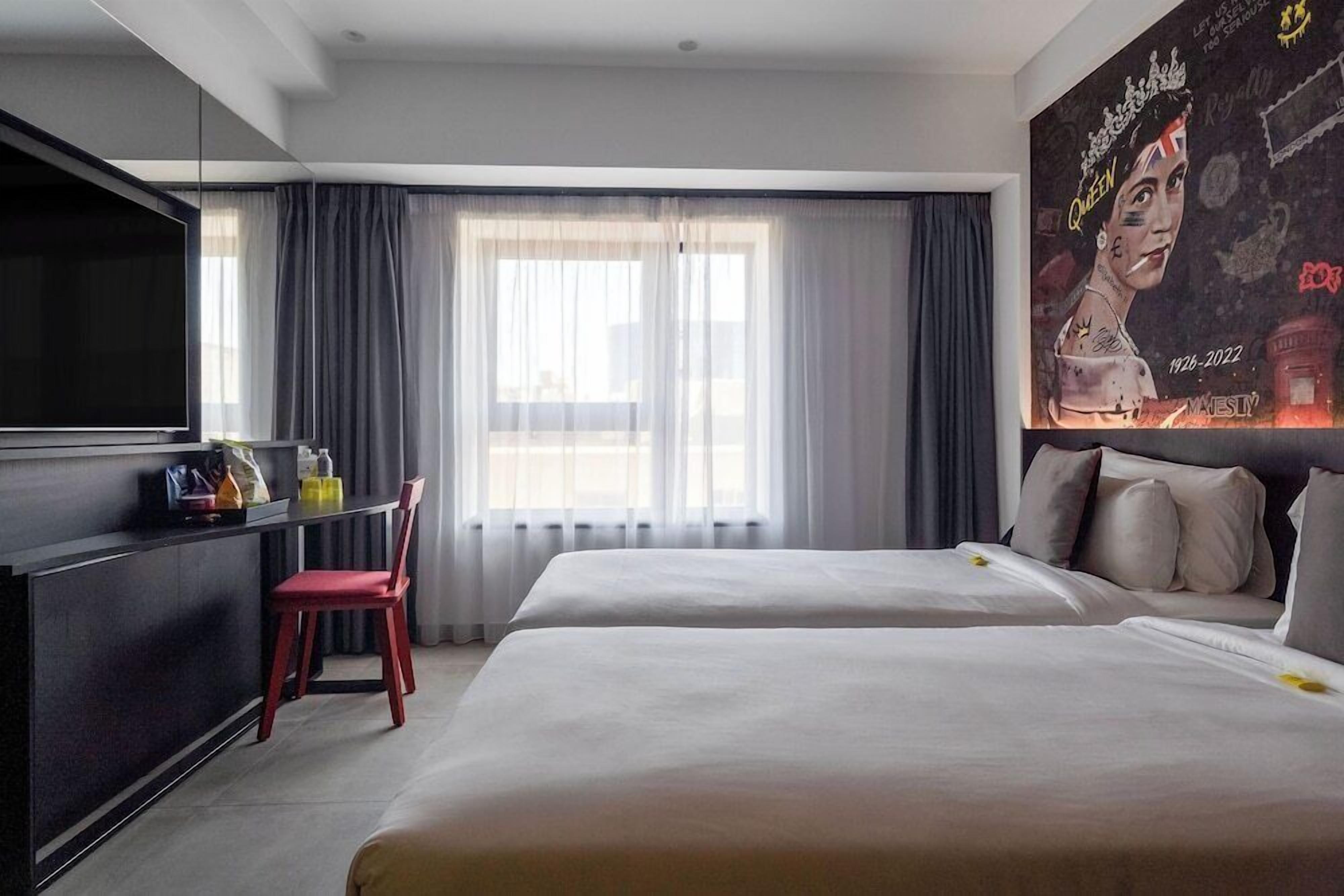 Ein Hotelzimmer mit zwei Betten, einem Fernseher, einem Schreibtisch und einem großen Fenster mit Vorhängen.