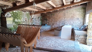 A stone-walled room with a hammock, a white cushioned bench, and a small table.