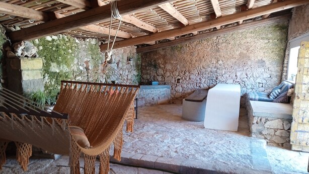 A stone-walled room with a hammock, a white cushioned bench, and a small table. - Characteristic olive grove (Noto)