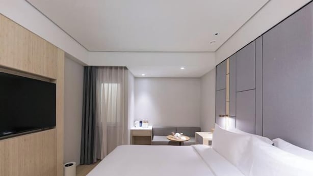 Ein modernes Hotelzimmer mit einem großen Bett, einem flachbildfernseher an der Wand, einem kleinen Nachttisch und einem Schreibtisch mit Stuhl.