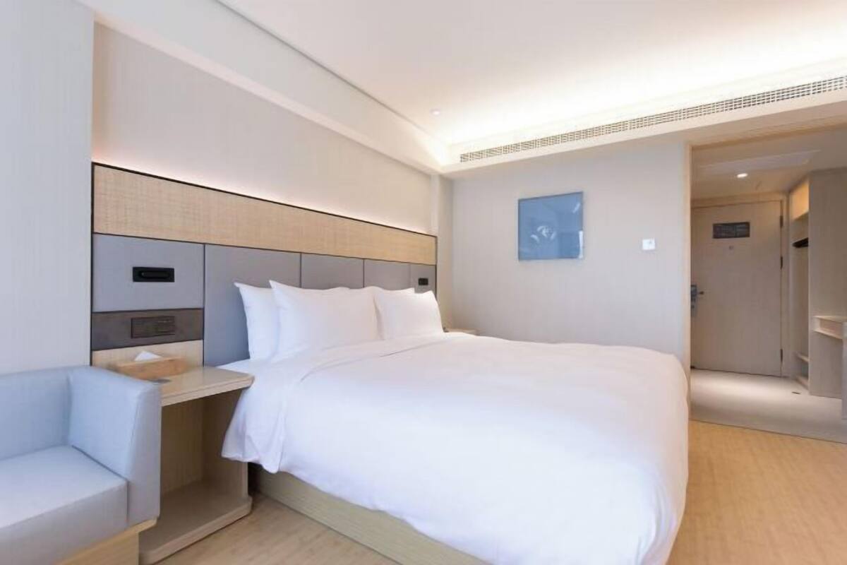 Una habitación de hotel moderna con cama, mesita de noche y un pequeño rincón de descanso.