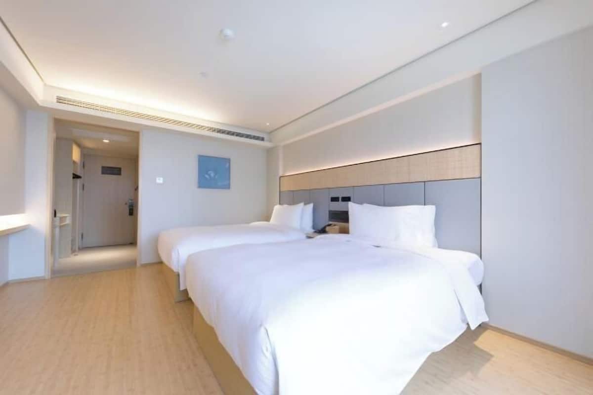Habitación de hotel con dos camas, suelo de madera, cabecera moderna y puerta que da a otra habitación.
