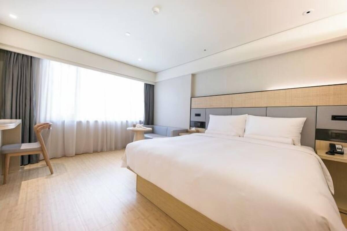 Una habitación de hotel moderna con una cama grande, un escritorio, una silla y una ventana con cortinas.