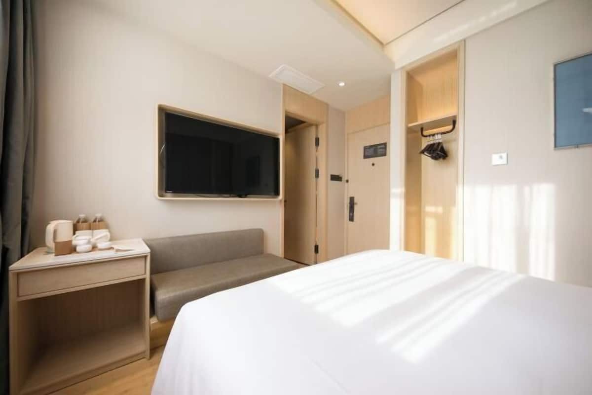 Habitación de hotel con una cama, un escritorio con silla, televisión y puerta que da a un baño.