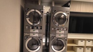 Zwei übereinander gestellte Waschmaschinen mit Frontlader in einem Waschraum, mit einem Holzschrank und Aufbewahrungsboxen.