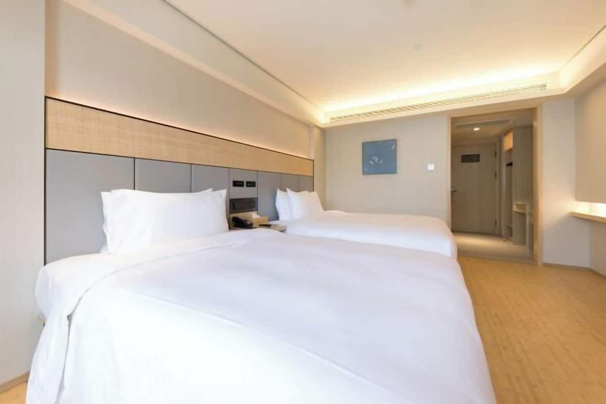 Habitación de hotel con dos camas, una mesita de noche, televisor montado en la pared y puerta que da a un baño.