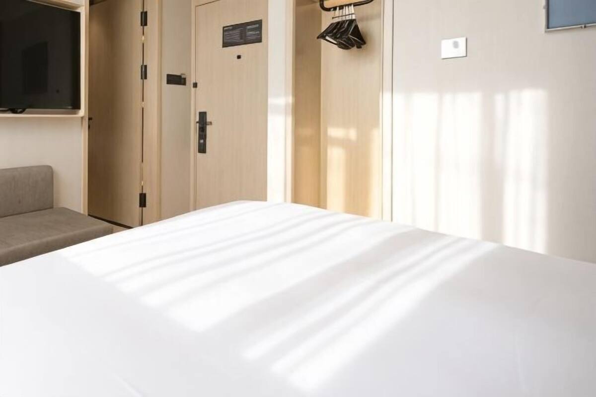 Una habitación de hotel con una cama, televisión, armario y perchero.