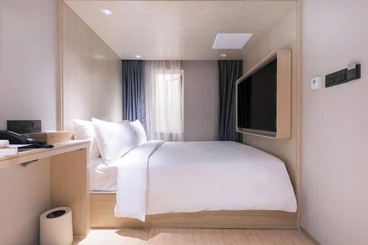 Una habitación de hotel con cama, escritorio, televisor y ventana con cortinas.