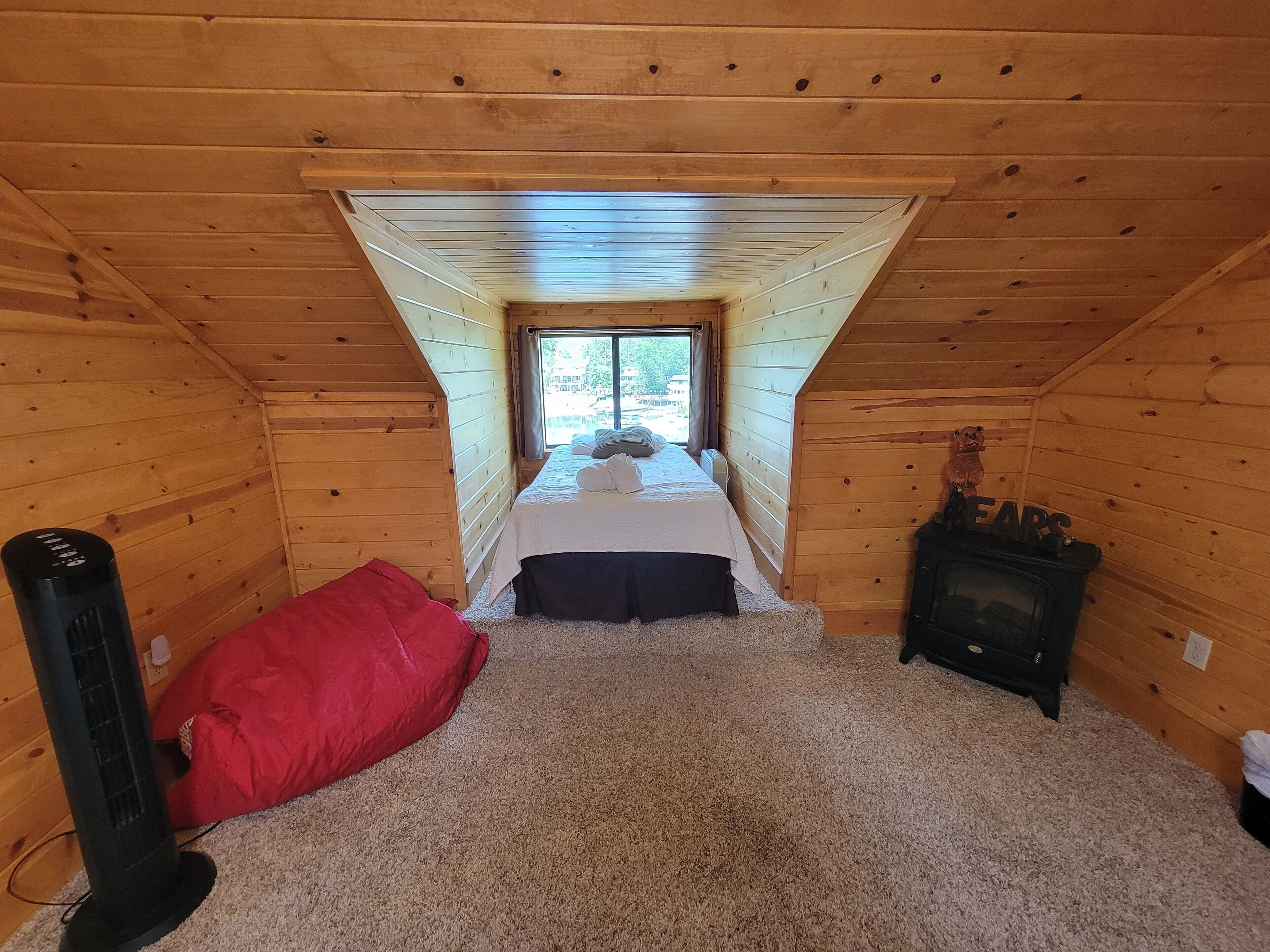 Ein gemütliches Schlafzimmer im Dachgeschoss mit schrägen Wänden, einem Bett mit weißer Bettwäsche, einem roten Kopfkissen, einem Heizgerät und einem Kamin.