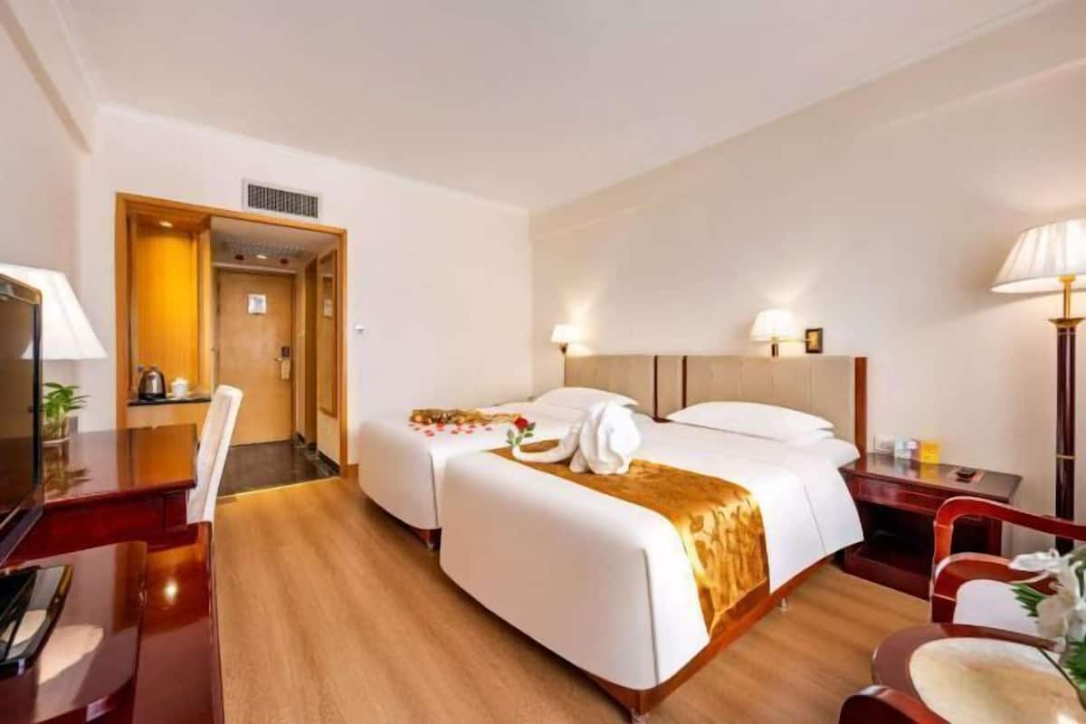 A hotel room with two beds, a desk, a chair, and a TV.