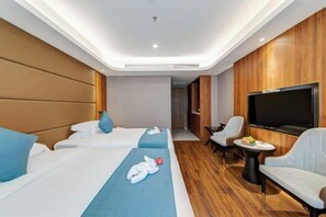 Une chambre d’hôtel avec deux lits, une télévision, un coin salon avec des fauteuils et un plancher en bois.