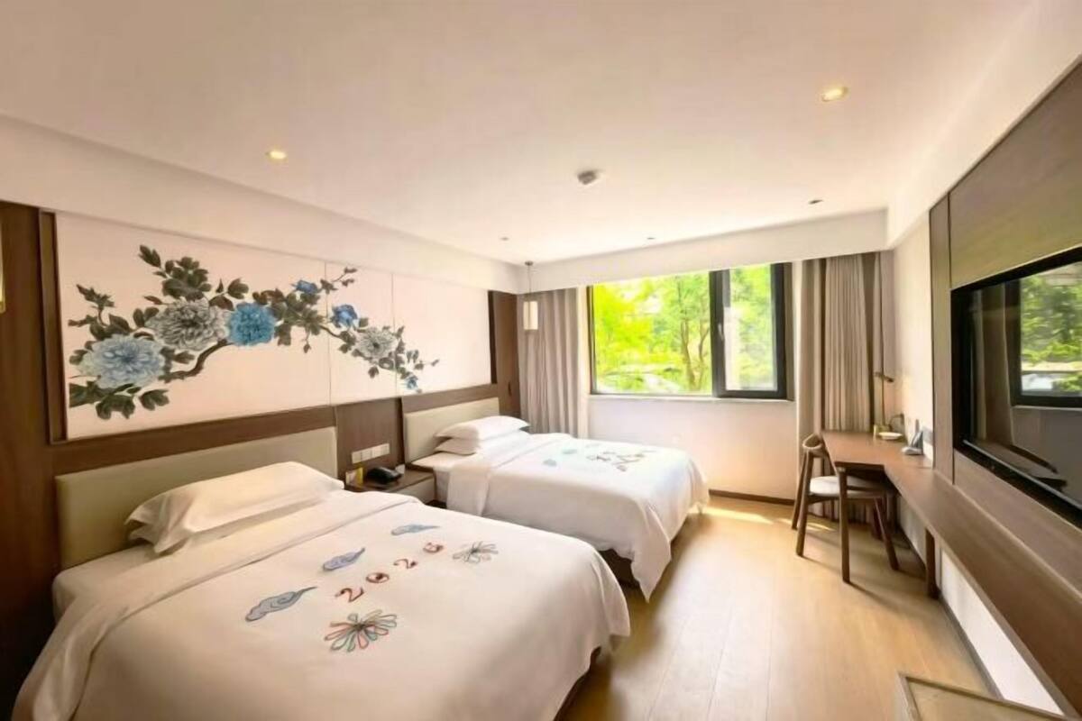 A hotel room with two beds, a desk, and a large window.