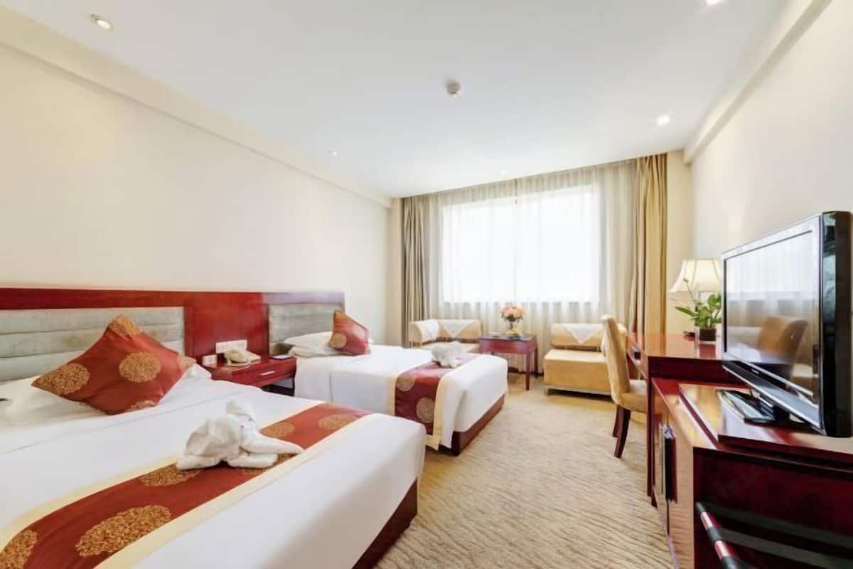 A hotel room with two beds, a TV, a desk, and a window with curtains.