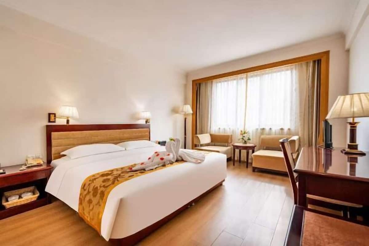 A hotel room with a large bed, a desk, a chair, a sofa, and a window with curtains.