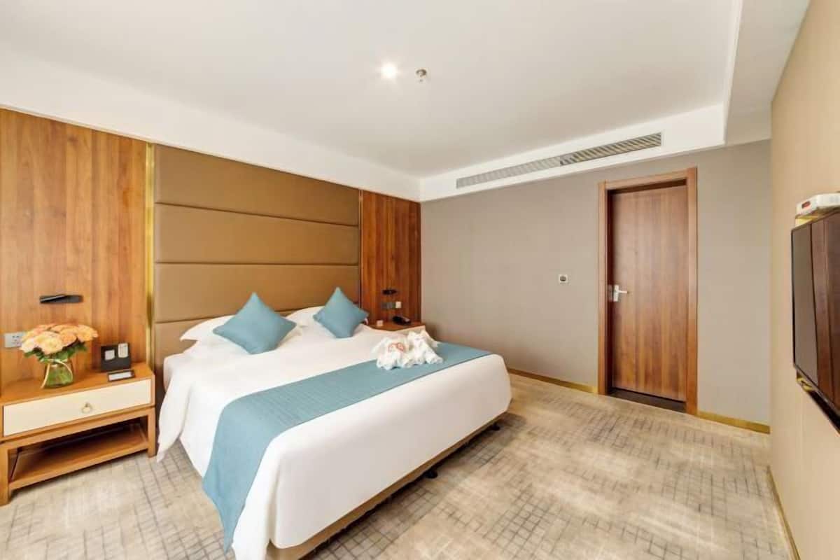 A hotel room with a bed, bedside tables, a nightstand, a dresser, a TV, and a door.
