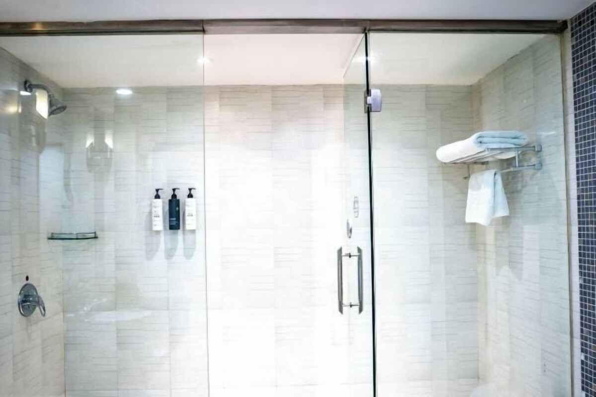 A modern bathroom with a glass shower enclosure, a towel rack, and toiletries on the wall.