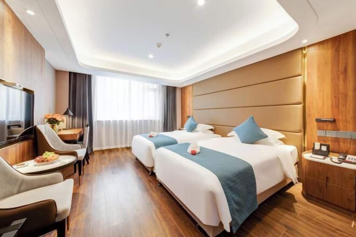 A hotel room with two beds, a desk, a chair, a TV, and a window with curtains.