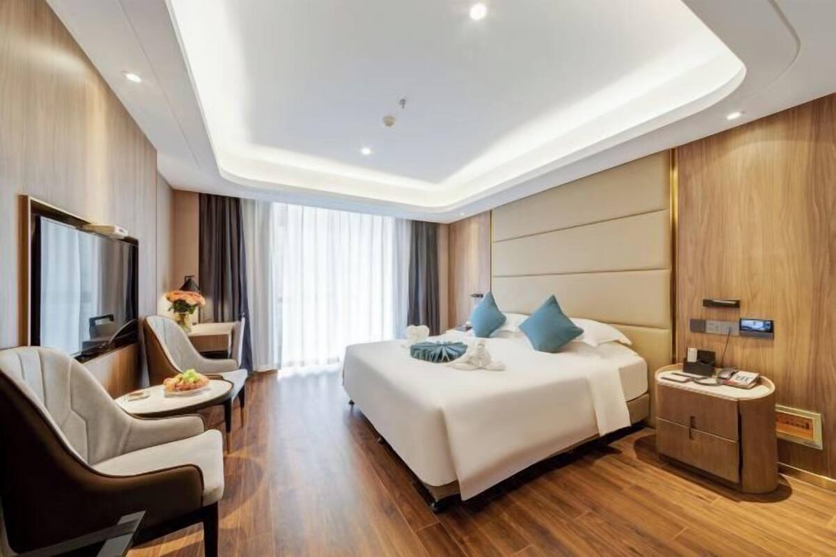 A modern hotel room with a large bed, a desk, a chair, and a TV.