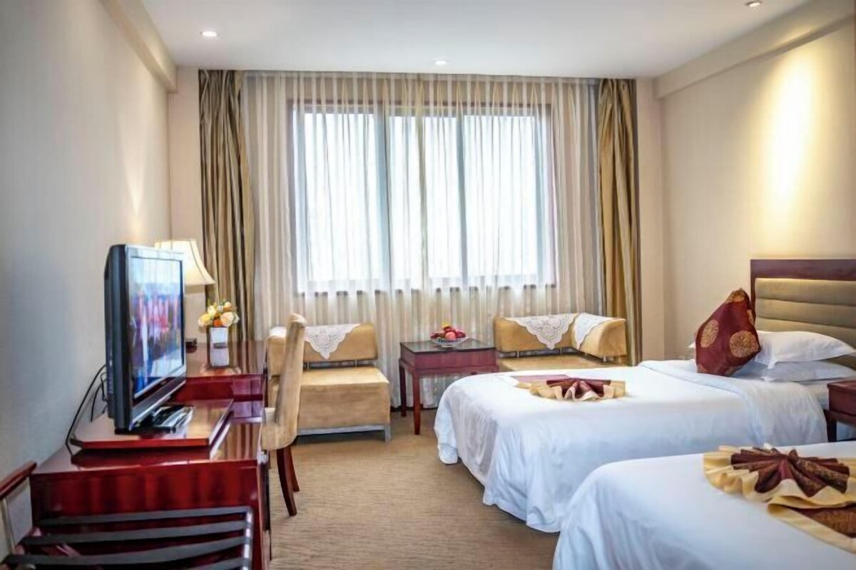 Ein Hotelzimmer mit zwei Betten, einem Schreibtisch mit Fernseher, einem Sessel und einem Tisch mit Lampe.