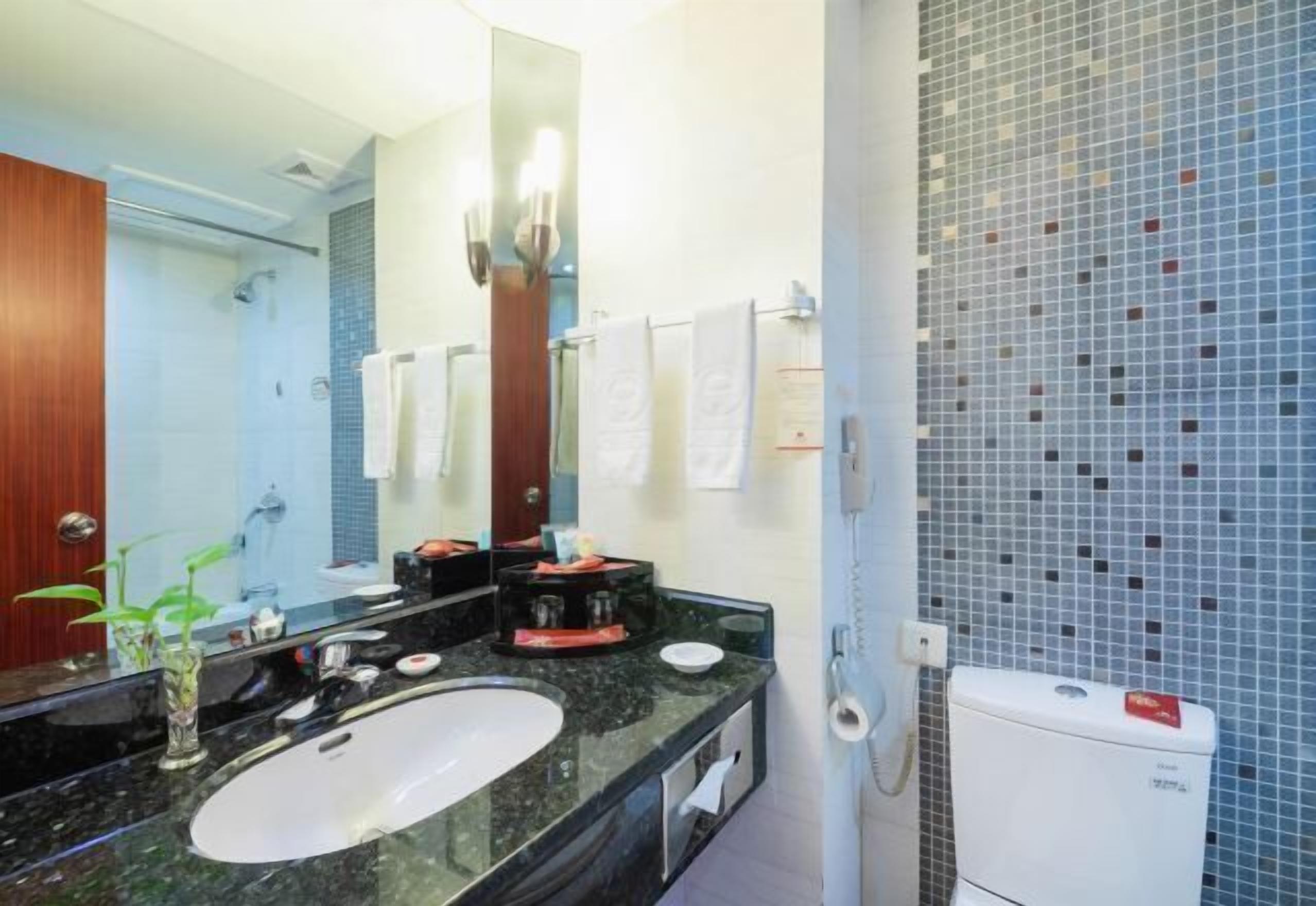 A bathroom with a large mirror, a sink, a toilet, and a shower.
