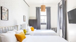 A hotel room with two beds, a TV, a lamp, and a window with curtains. - Inn at Gough (San Francisco)