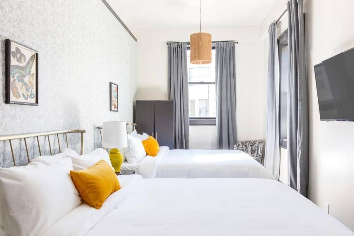 A hotel room with two beds, a TV, a lamp, and a window with curtains.