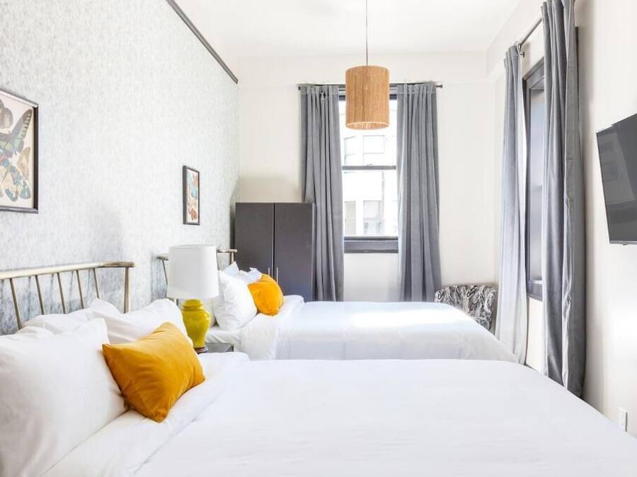 Habitación de hotel con dos camas, televisión, lámpara y ventana con cortinas.