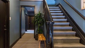A hallway with a carpeted floor, a wooden bench, a potted plant, and a staircase with a black railing. - Inn at Gough (San Francisco)