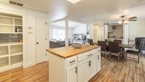 A modern kitchen with white cabinetry, a wooden countertop, and a dining area with a table and chairs. - Entire Home Away From Home (Meridian)