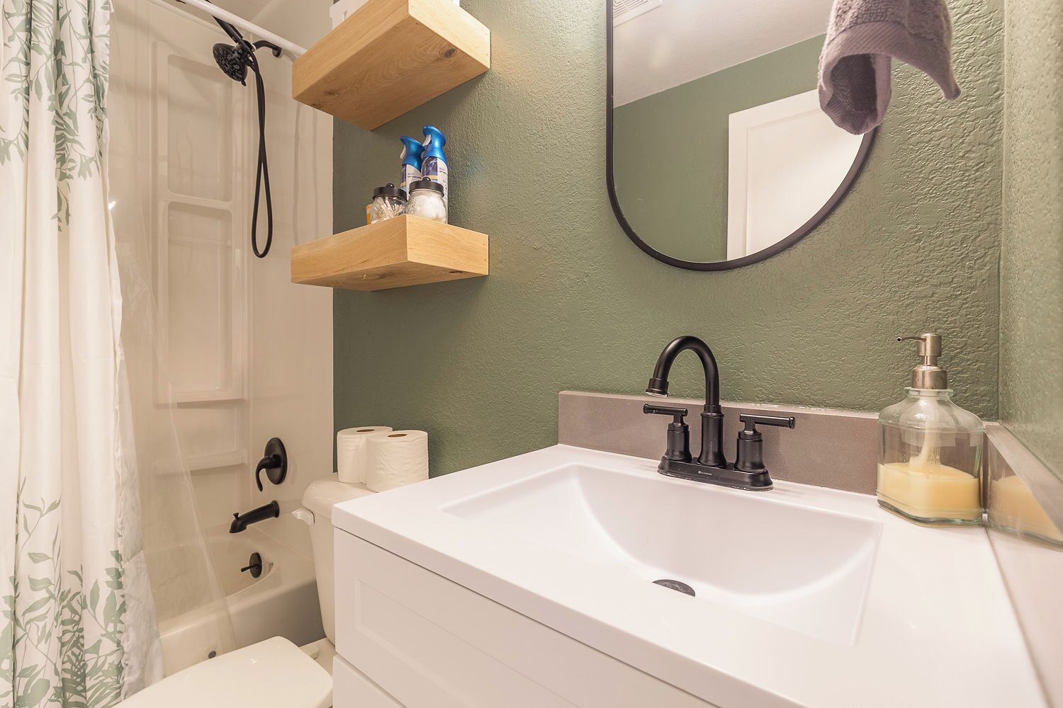 A bathroom with a white sink, a mirror, a shower, and a towel hanging on the wall.