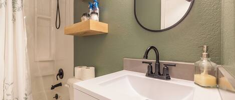 A bathroom with a white sink, a mirror, a shower, and a towel hanging on the wall.