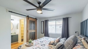A bedroom with a bed, a ceiling fan, a window with curtains, and a door leading to a bathroom. - Entire Home Away From Home (Meridian)