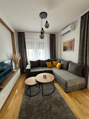 Una sala de estar moderna con un sofá modular, dos mesas redondas de centro, un televisor de pantalla plana y un ventanal con cortinas translúcidas.