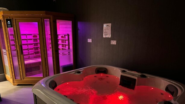 A spa area with a hot tub and two wooden cabinets with purple lighting. - Heart of Hull Hotel (Hull)