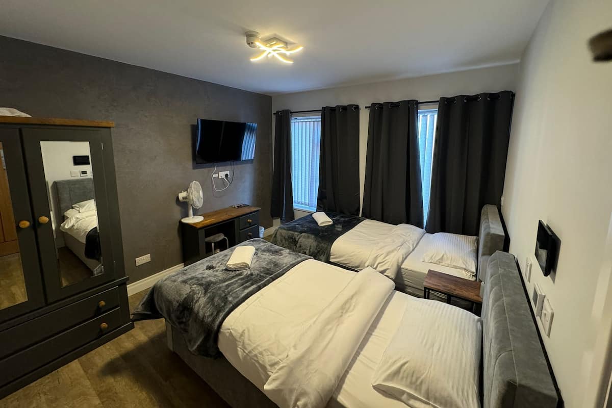 A hotel room with two beds, a TV, a desk with a chair, a mirror, and a ceiling fan.