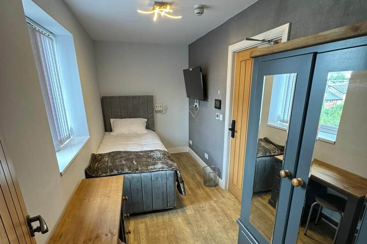 A compact room with a bed, a desk, a wardrobe, and a mirror.