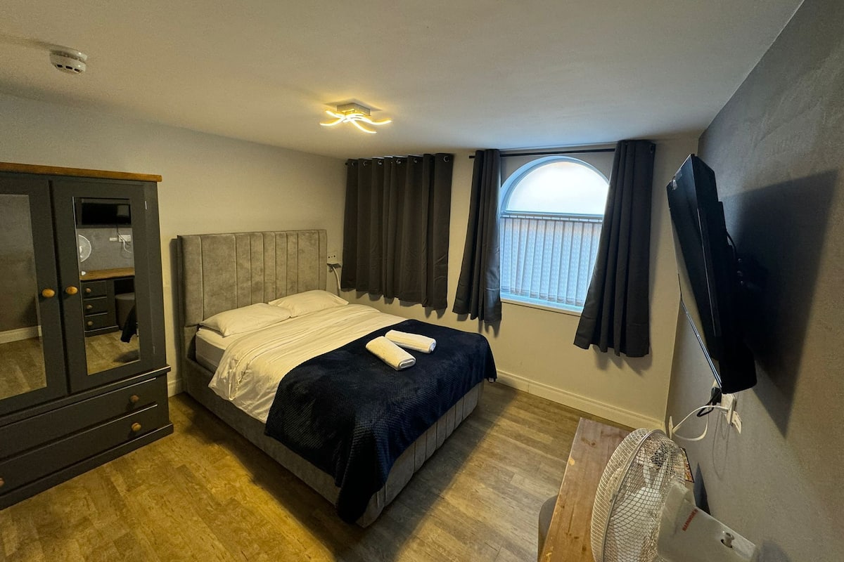 A bedroom with a bed, a wardrobe, a TV, a window with curtains, and a ceiling light.