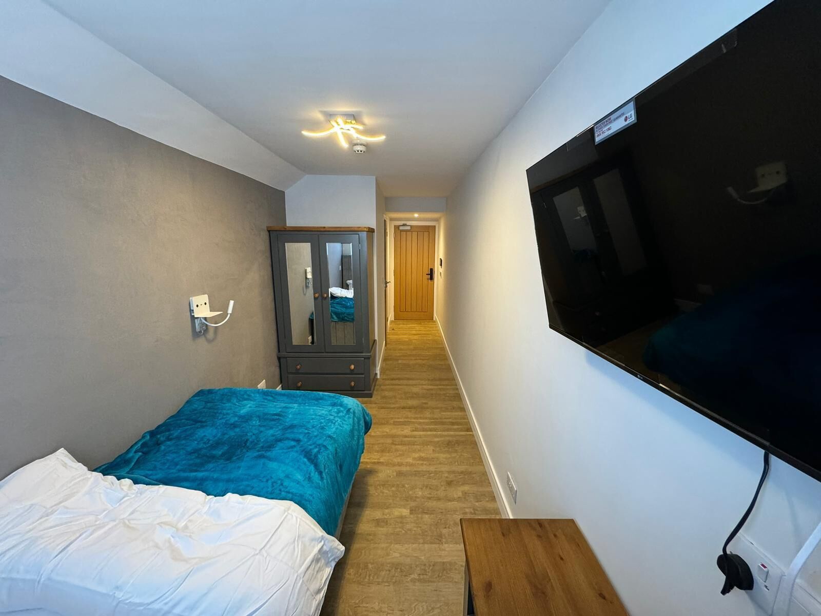 A bedroom with a bed, a wardrobe, a TV, and a hallway leading to another room.