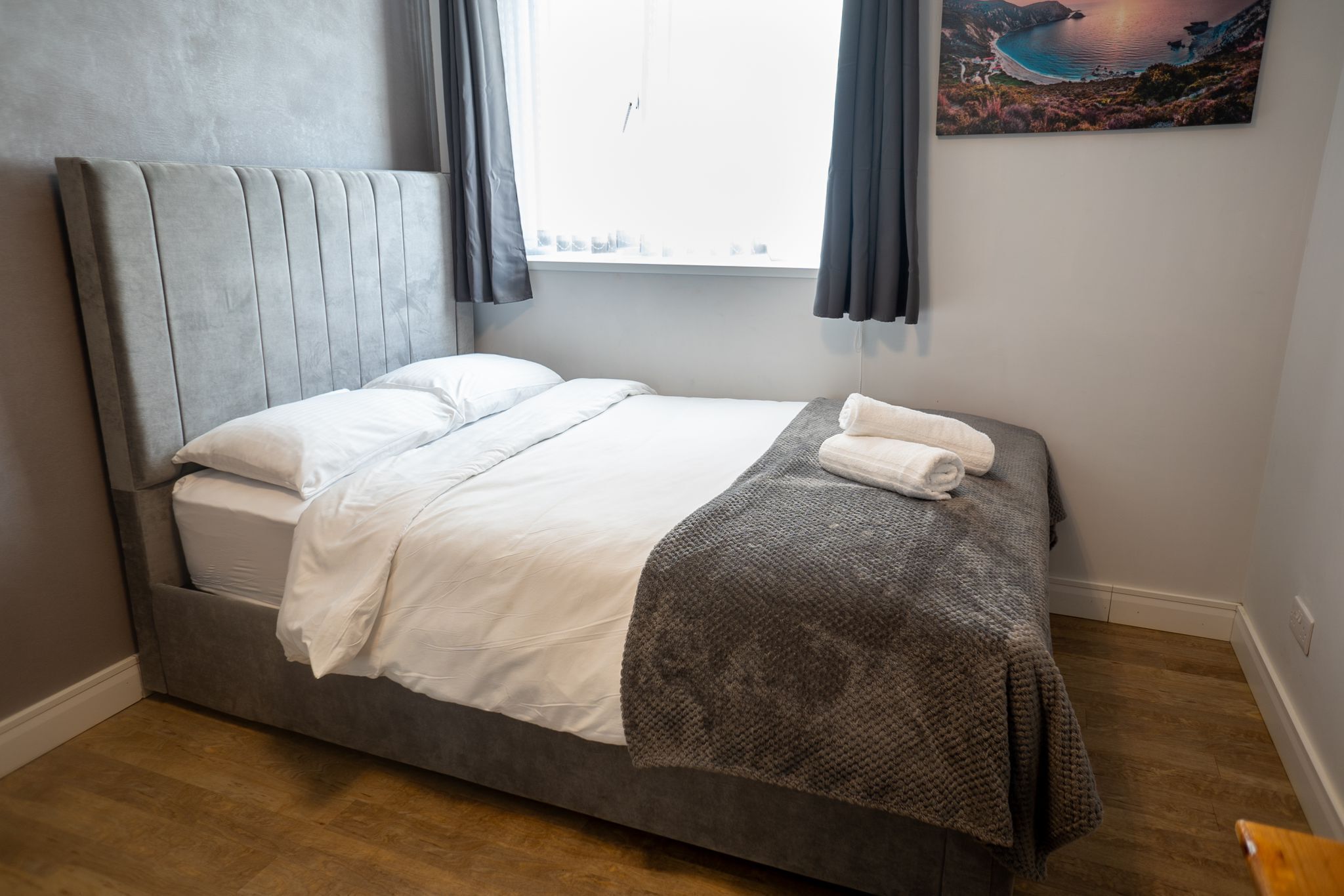 Un letto rifatto con un comodo poggiatesta grigio, lenzuola bianche e una coperta grigia.